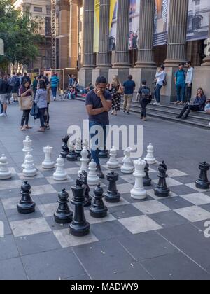 Menschen Schach spielen auf grossen Pflaster Schachbrett vor der Staatsbibliothek von Victoria mit Bibliothek spalten und Banner im Hintergrund. Stockfoto