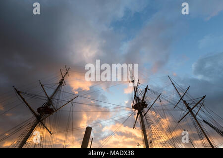 Vibrant orange Wolken in einem dramatischen Himmel über der hölzernen Masten der HMS Gannet Im Historic Dockyard, Chatham, Kent, Großbritannien kurz vor Sonnenuntergang. Stockfoto