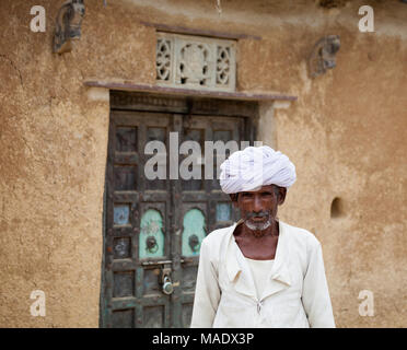 Rajasthani-Mann in weißem Turban und traditioneller Kleidung, fotografiert vor einem schlammigen Gebäude, das im typischen Dorfstil entworfen wurde. Stockfoto