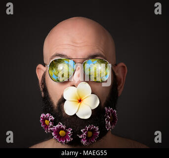 Spaß Portrait von kahlen unrasierten Mann mit Bart und Schnurrbart mit Chrysanthemen und Magnolia Blumen und Sonnenbrille mit Palmen auf dunklem Hintergrund Stockfoto