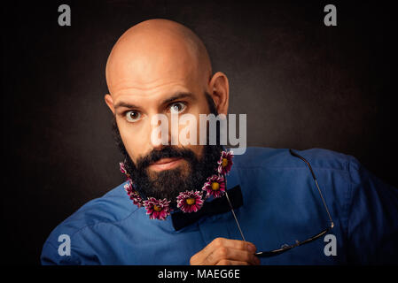 Portrait von unrasierten Mann mit Bart und Schnurrbart mit chrysantheme Blumen und Sonnenbrille auf dunklen vintage Hintergrund Stockfoto
