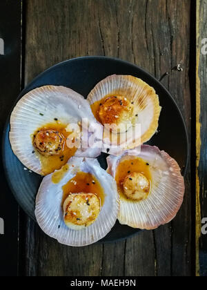 Riesige gegrillte frische tasmanische Jakobsmuscheln mit frischer Butter auf schwarze Platte Stockfoto