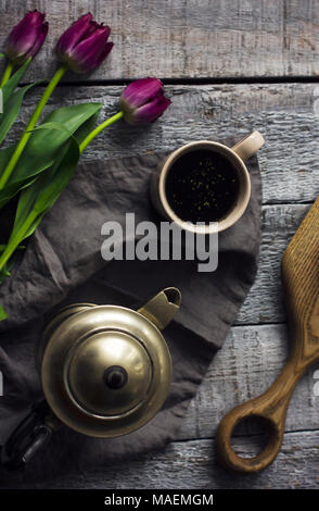 Stillleben mit Kräutertee, Metall Teekanne und Tulpen auf grau Holz- Hintergrund Stockfoto