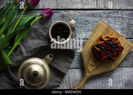 Stillleben mit Kräutertee, Brötchen mit Beeren und Tulpen auf grau Holz- Hintergrund Stockfoto