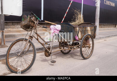 Peking, China - 26. April 2010: Nahaufnahme von Street Sweeper braun Metall Dreirad mit seinem Besen, entlang der Straße geparkt. Schwarz und Violett Wand. Stockfoto