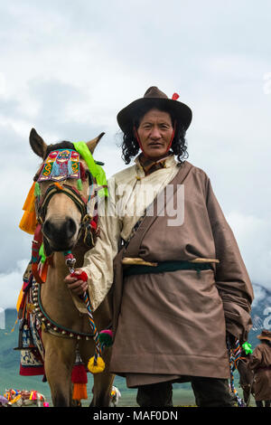 Tibetische Mann mit Pferd in traditioneller Kleidung bei Pferderennen Festival, Litang, westliches Sichuan, China Stockfoto