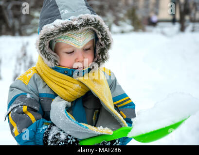 Wenig junge spielt mit Schnee und Spaten. Baby spielt mit Schnee im Winter im Freien. Winter Urlaub. Kinder winter Spiele im Freien. Stockfoto
