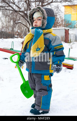 Wenig junge spielt mit Schnee und Spaten. Baby spielt mit Schnee im Winter im Freien. Winter Urlaub. Kinder winter Spiele im Freien. Stockfoto