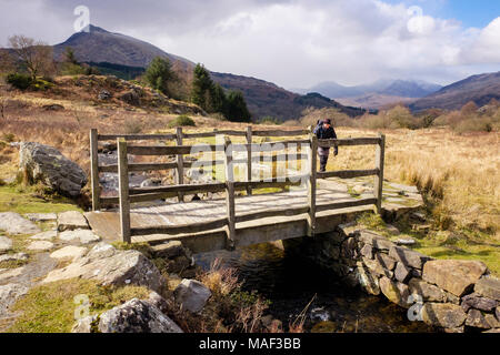 Wanderer auf ein Land zu Fuß nähern Holzsteg Überquerung eines Datenstroms auf einem Wanderweg in Snowdonia National Park. Capel Curig Conwy Wales UK Großbritannien Stockfoto