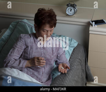 Ältere Frau, die Einnahme von Medikamenten während der Nacht im Bett Stockfoto
