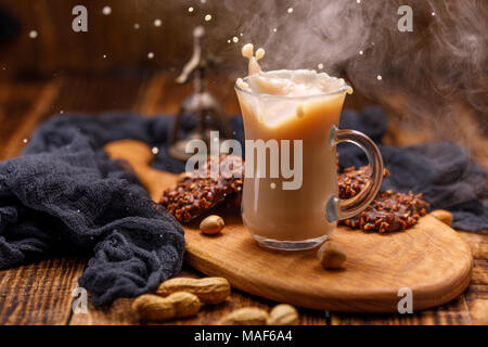 Rauchen, Kaffee mit Milch und Schokolade Kekse mit Muttern zum Frühstück sind von der Schale verschüttet. Tee mit Gebäck in ein Glas Schale mit einem Splash. Stockfoto