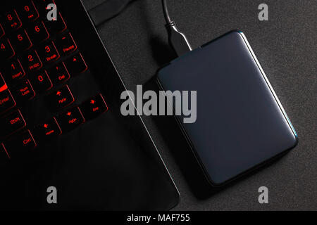Eine externe Festplatte an den Laptop mit einem USB-Kabel auf einem schwarzen Hintergrund verbunden. Stockfoto