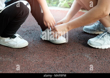 Mutter hilft, seinen Sohn, seine Schuhe im Park mit Kopie Raum zu binden. Stockfoto