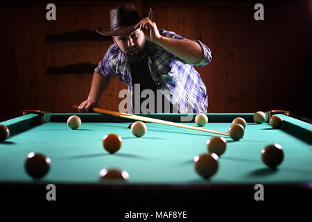 Ein Mann mit einem Bart spielt eine große Billard. Partei in 12-Fuß-Pool. Billard im Club Spiel für Männer. Ein Mann mit einer Cue bricht die Pyramide. Stockfoto