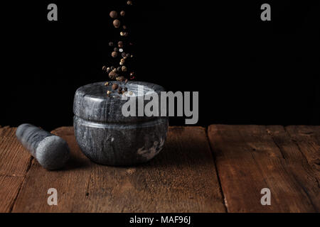 Marmor mörser auf alten Holztisch auf schwarzen Hintergrund mit kopieren. Pepper Samen fallen in den Mörtel. Gefrierschrank essen. Stockfoto