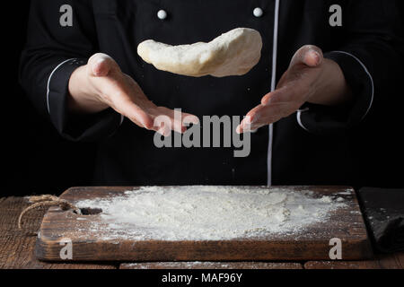 Eine Frau Koch wirft einen Hefeteig in ihre Hände auf einem schwarzen Hintergrund. Stockfoto