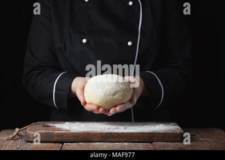 Köchin holding Hefeteig in ihren Händen auf schwarzem Hintergrund. Stockfoto