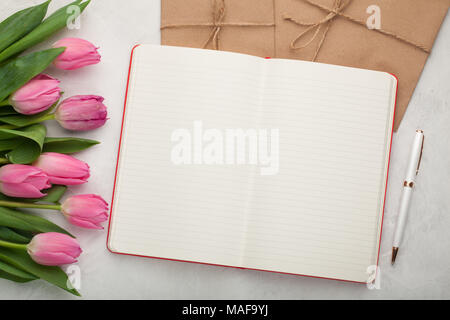 Leere Notizblock mit Kugelschreiber, Umschläge und rosa Tulpen auf hellem Stein Hintergrund. Stockfoto