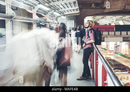 Hipster bärtigen Mann in den Bahnhof mit Menschen Bewegung Hintergrund, während in der Nacht unterwegs. Stockfoto