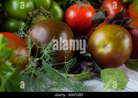 Grüne und rote Farbe Gemüse, schwarzen und roten Tomaten, grüne und rote Paprika, duftende Kräuter auf einem alten Holztisch, Ansicht von Oben, kopieren Raum Stockfoto