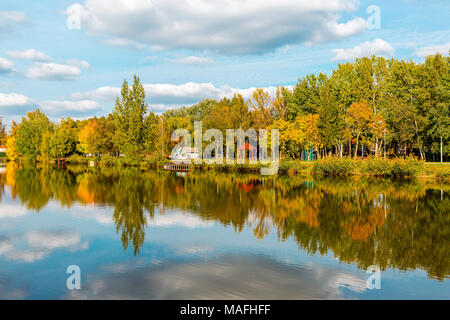 Schönen See mit Spiegel Reflexionen im klaren Wasser an einem sonnigen Tag. Ruhige Landschaft mit See, bewölkter Himmel, und Bäume symmetrisch spiegelt sich in der Stockfoto