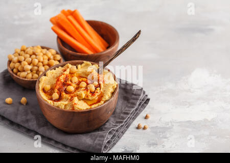 Hummus, frische Karotten Sticks und gekochte Kichererbsen in hölzernen Schüsseln. Vegane Ernährung Konzept, hellen Hintergrund Stockfoto