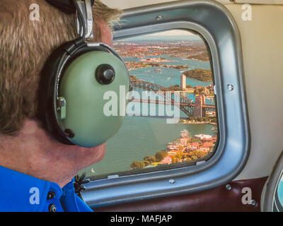 Blick aus dem Flugzeug Fenster über den Hafen von Sydney Australien fliegen. Eine touristische Mann sieht, das Tragen von Gehörschutz. Stockfoto