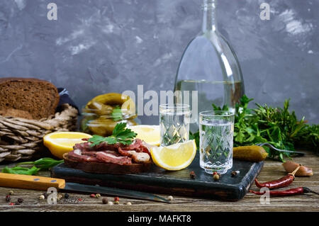 Zwei Shot Gläser Wodka mit Zitronenscheibe, Gewürzgurken und Roggenbrot mit gesalzener Speck auf dem dunklen Hintergrund. Traditionelle starkes Getränk und App Stockfoto