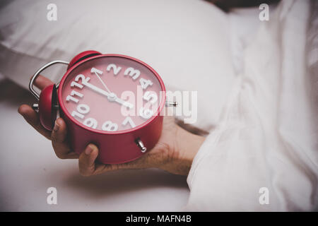 Mann im Bett, der Wecker um 6 Uhr. Stockfoto