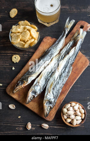 Verschiedene Snacks für Bier: Sonne getrockneten Fisch, Nüsse, gesalzen Croutons oder Cracker über Holz- Hintergrund, Ansicht von oben, kopieren. Lagerbier und Snacks mit d Stockfoto