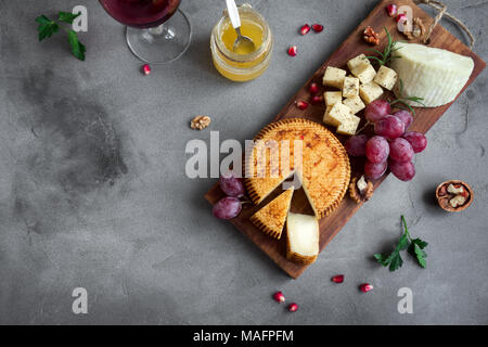 Käseplatte mit verschiedenen Käsesorten, Trauben, Nüsse über konkreten Hintergrund, kopieren. Italienischen Käse und Obstteller mit Honig und Wein. Stockfoto