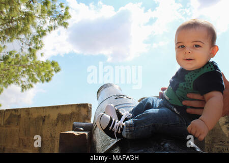 Sechs Monate altes Baby Junge sitzt auf dem Canon mit Hilfe von DADY Stockfoto