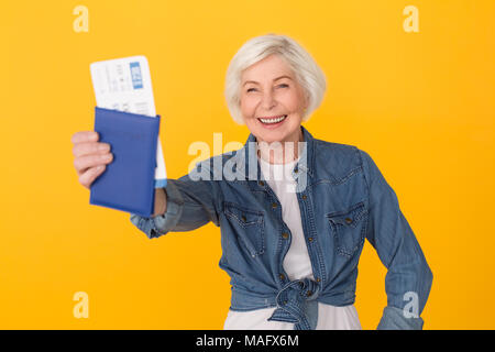 Im Alter von weiblichen Reisenden Studio auf gelben Hintergrund holding Pass und Ticket schließen isoliert, lächeln, glücklich Stockfoto