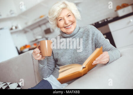 Glück ältere Frau liest das Buch am Morgen und trinkt Kaffee. Innen-, Studio schießen, Home Interior Stockfoto