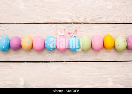 Objekte Ostern bunte Eier auf Holz- Hintergrund in einer Reihe isoliert in der Mitte mit kleinen süßen Hasenohren und Papier Butterfly Top View eingerichtet Stockfoto