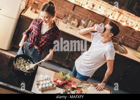 Mann trinkt Kaffee am Morgen, während seine Frau bereitet ihm das Mittagessen für die Arbeit. Hallenbad, Küche Home Interior, Studio gedreht. Stockfoto