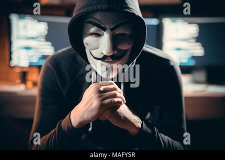 Junger Mann finanzielle Hacker im Büro sitzen tragen vendetta Maske suchen Kamera gefährlich Stockfoto