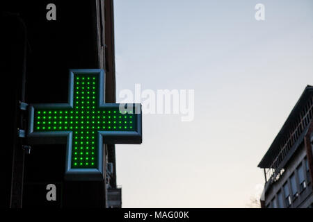 Apotheke Green Cross beleuchtet mit Neon und LED-Leuchten in den Sonnenuntergang. Dieses Kreuz ist ein universelles Symbol für Apotheke in Europa Bild von einem grünen Kreuz Anzeige Stockfoto