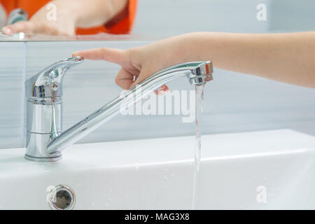 Die Hand des Kindes schließt das Wasser aus dem Mixer, indem Sie die Finger am Griff Stockfoto