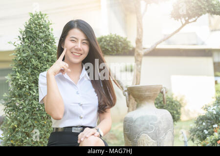 Nette junge asiatische Frau in Uniform student Lächeln in Garten, Glücklich und Konzept entspannen Stockfoto