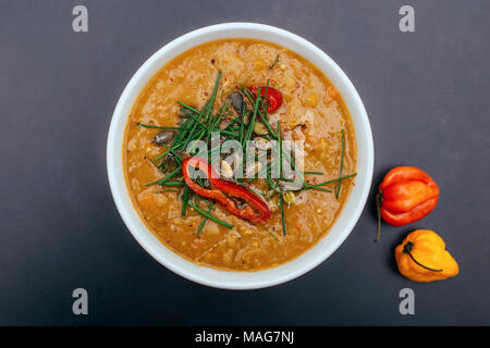 Weiße Schüssel einer gesunden vegetarischen Erbsensuppe mit Kürbiskernen, Schnittlauch und würzig Chili. Farbe Orange, schwarzer Hintergrund, dunklen Essen Fotografie Stockfoto