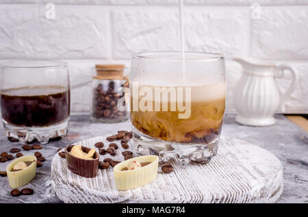 Gießen Milch in ein Glas heißes starken Kaffee Schokolade Süßigkeiten und Kaffee latte Zubereitung Bewegung von Flüssigkeiten im Glas Stockfoto