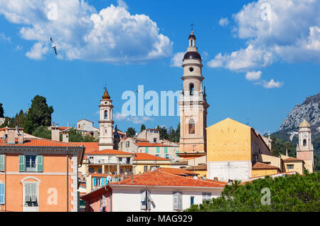 Blick auf Kirche Glockenturm unter bunten Häusern unter blauem Himmel in kleinen Städtchen Menton in Frankreich. Stockfoto