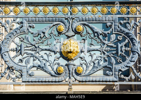 Nahaufnahme der schmiedeeisernen Geländer des Balkons Pariser Gebäude mit einem Golden Lion's Head in der Mitte durch pflanzliche umgeben dekoriert Stockfoto