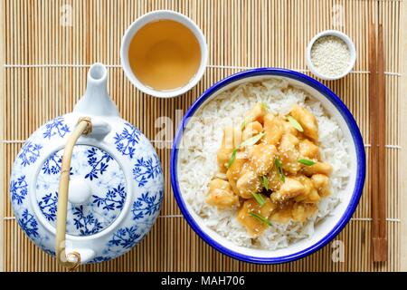 Chinesische orange Huhn mit Reis, China Teekanne und Tasse grünen Tee auf Bambus Hintergrund. Ansicht von oben. Traditionelle chinesische Küche Stockfoto