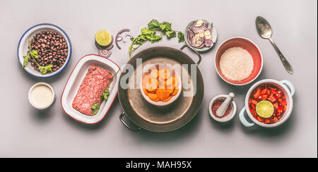 Schalen mit Zutaten für eine ausgewogene Mahlzeit eine Pfanne mit Bohnen, Hackfleisch, Reis und Gemüse auf grauem Hintergrund, Ansicht von oben, flach Stockfoto