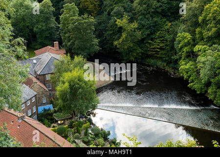 Hohes Ansehen von Wasser über Wehr über den Fluss Nidd & historisches Schloss Mühlen, eine alte Textilfabrik zu Wohnungen - Knaresborough, England, Großbritannien konvertiert fließt. Stockfoto