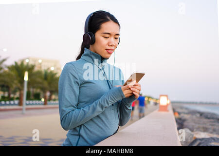 Mädchen mit Telefon und Musik hören mit Kopfhörern auf dem Boardwalk Stockfoto