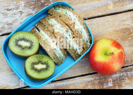 Braun creme Käse und Gurke Sandwiches in Lunch Box, Kiwi und Apple Stockfoto