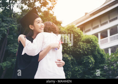 Junge weibliche Absolventin und umarmte ihre Mutter an der Abschlussfeier, Erfolg, Ziel. Bildung Konzept. Stockfoto